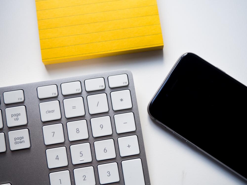 Keyboard, Phone, and Yellow Note on White Desk Keyboard, Phone, and Yellow Note on White Desk