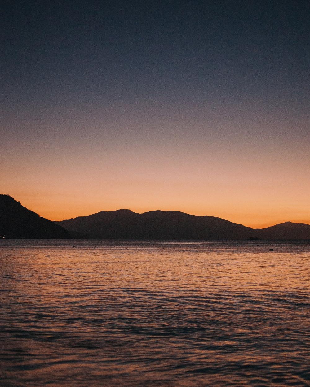 The Sun Sets Behind The Silhouette Of Seaside Mountains Photo The Sun Sets Behind The Silhouette Of Seaside Mountains Photo