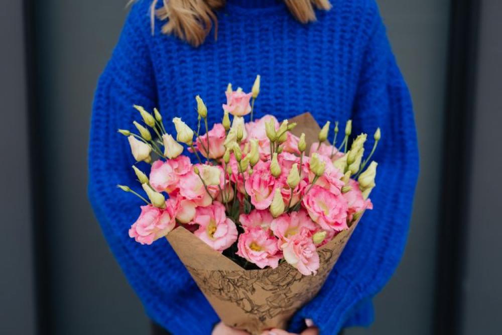 Close up of woman holding bouquet of pink lisianthus flowers wrapped in brown paper Close up of woman holding bouquet of pink lisianthus flowers wrapped in brown paper