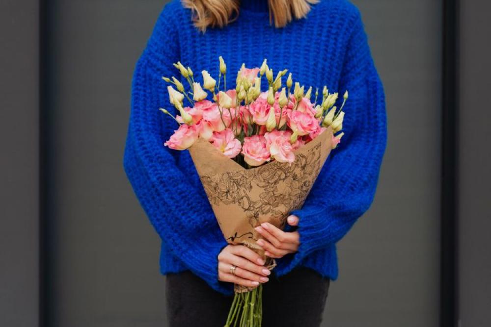 Close up of woman holding bouquet of pink lisianthus flowers wrapped in brown paper Close up of woman holding bouquet of pink lisianthus flowers wrapped in brown paper