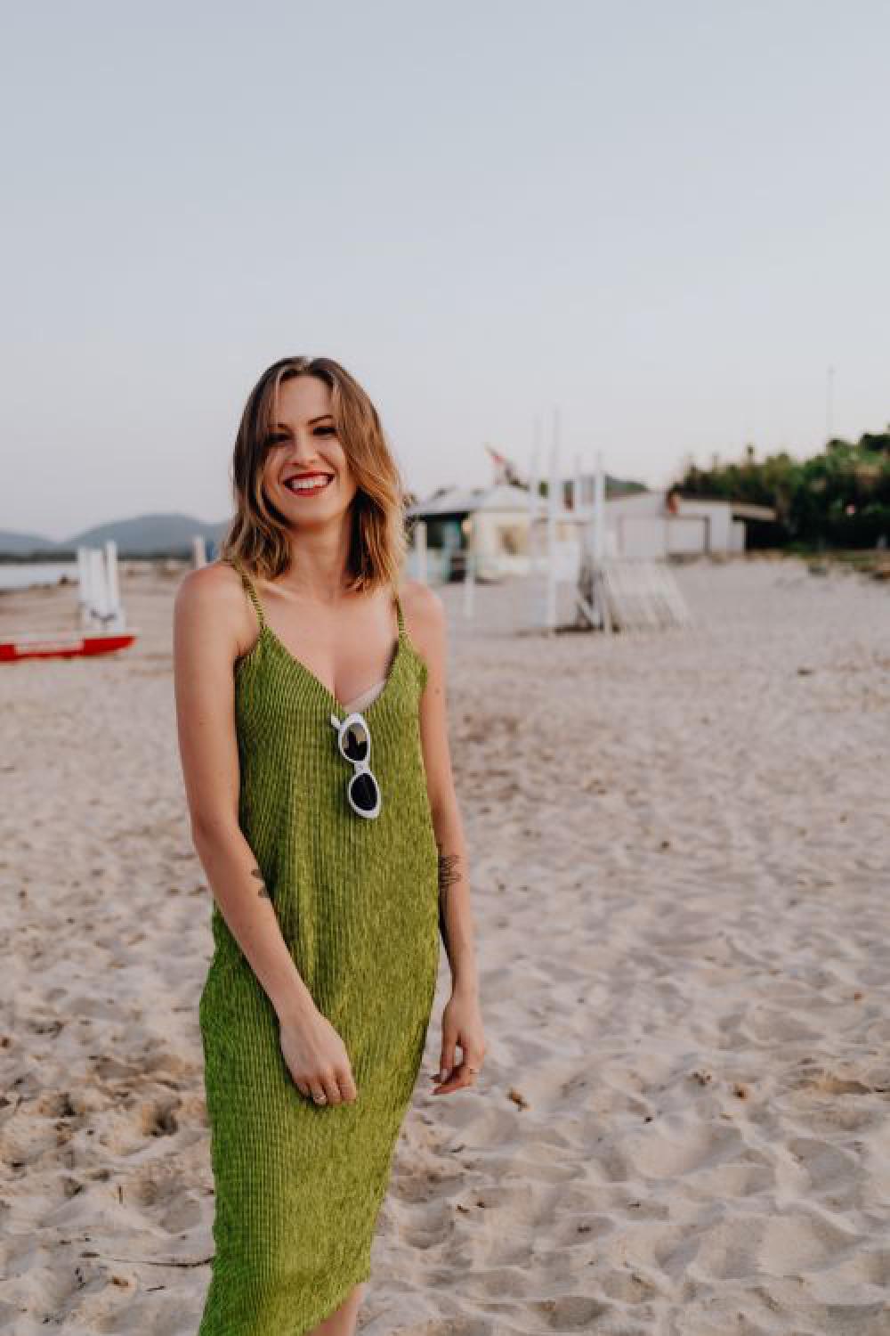 A woman in a green dress on the beach with white sunglasses A woman in a green dress on the beach with white sunglasses