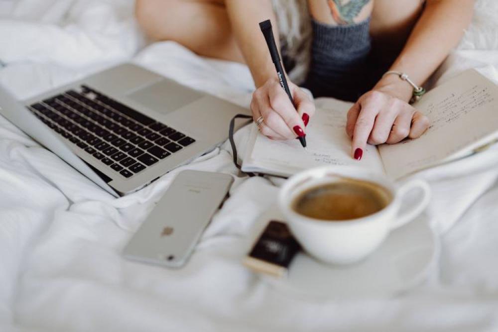 Woman working on a laptop while enjoying a breakfast coffee and chocolate in bed Woman working on a laptop while enjoying a breakfast coffee and chocolate in bed