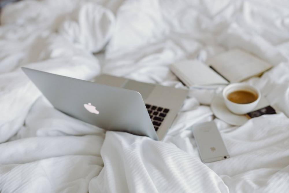 Woman working on a laptop while enjoying a breakfast coffee and chocolate in bed Woman working on a laptop while enjoying a breakfast coffee and chocolate in bed
