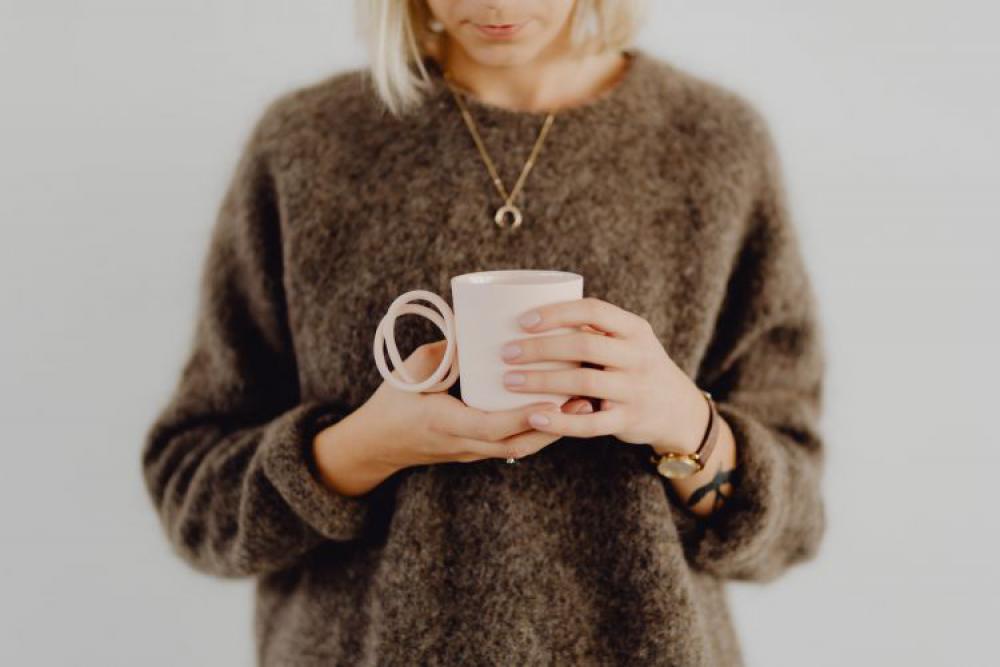 A woman in a brown sweater holds a pink, minimalist mug A woman in a brown sweater holds a pink, minimalist mug