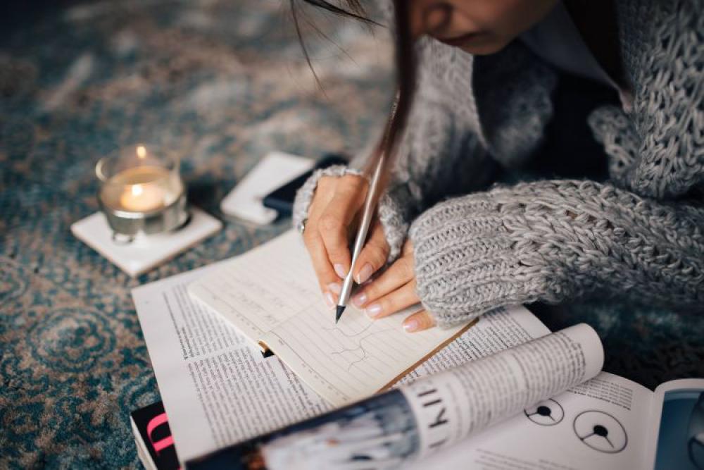 Woman in a grey sweater taking notes in an organizer Woman in a grey sweater taking notes in an organizer