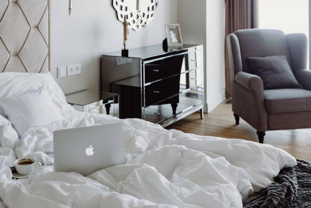 Woman working on a laptop while enjoying a breakfast coffee and chocolate in bed Woman working on a laptop while enjoying a breakfast coffee and chocolate in bed
