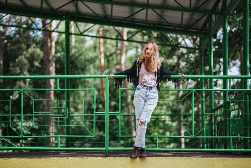 Blonde woman in a black jacket and ripped jeans by a green handrail Blonde woman in a black jacket and ripped jeans by a green handrail