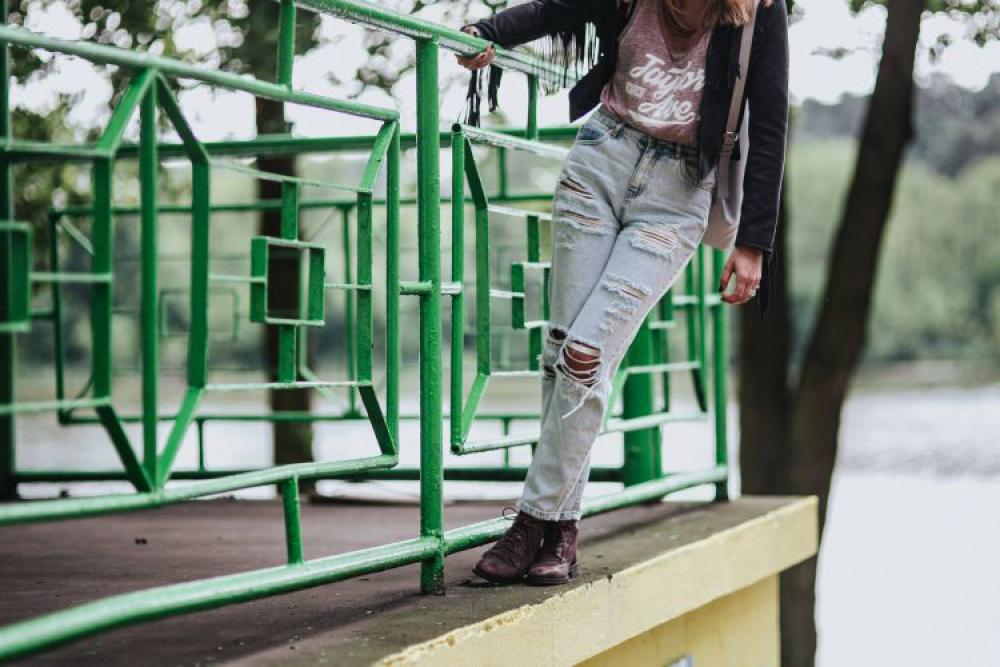 Blonde woman in a black jacket and ripped jeans by a green handrail Blonde woman in a black jacket and ripped jeans by a green handrail