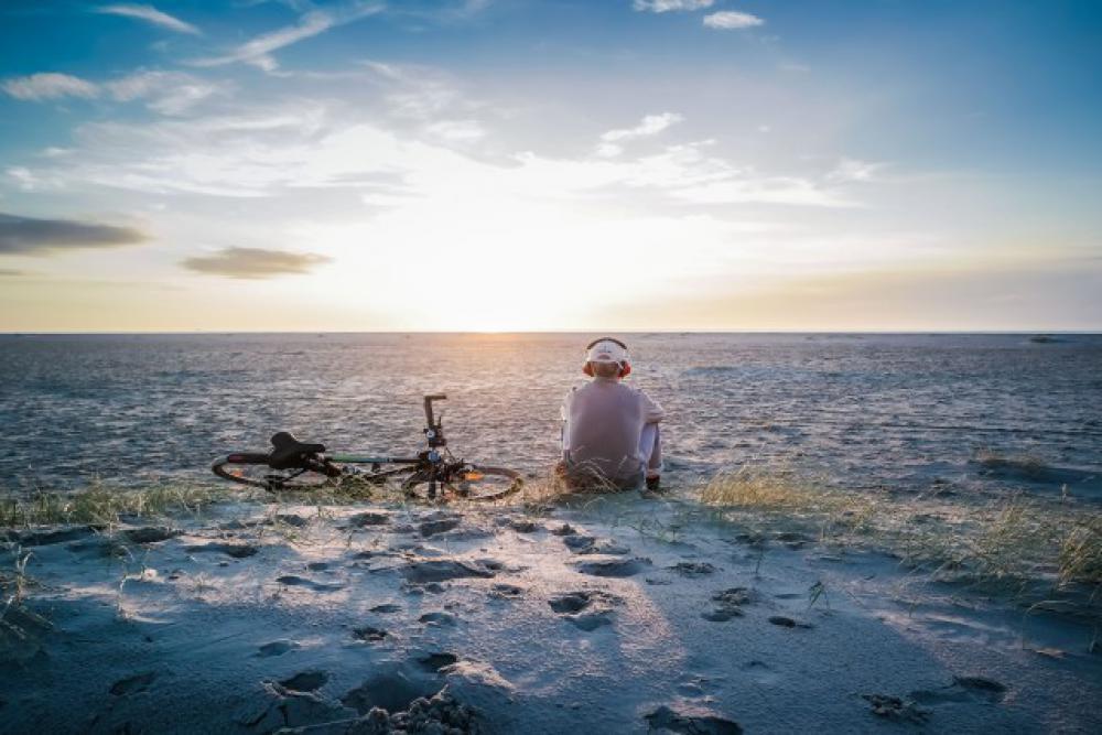 Young man sitting on the beach listen to Some music thruw his headphone and next to HIM lay his bike Young man sitting on the beach listen to Some music thruw his headphone and next to HIM lay his bike