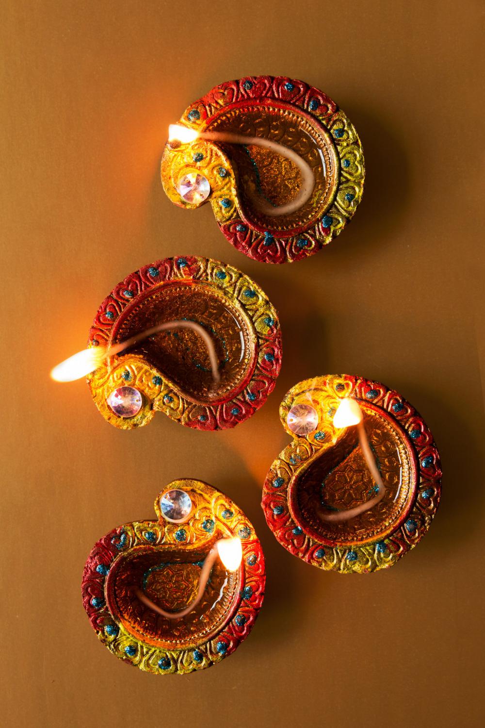 Four Candlelit Diya Lamps Rest On Brown Background Photo Four Candlelit Diya Lamps Rest On Brown Background Photo