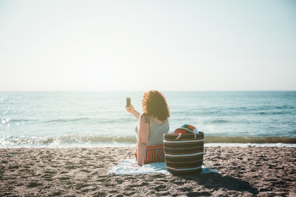 Young Woman Takes Selfie While Sitting On Sunny Beach Photo Young Woman Takes Selfie While Sitting On Sunny Beach Photo