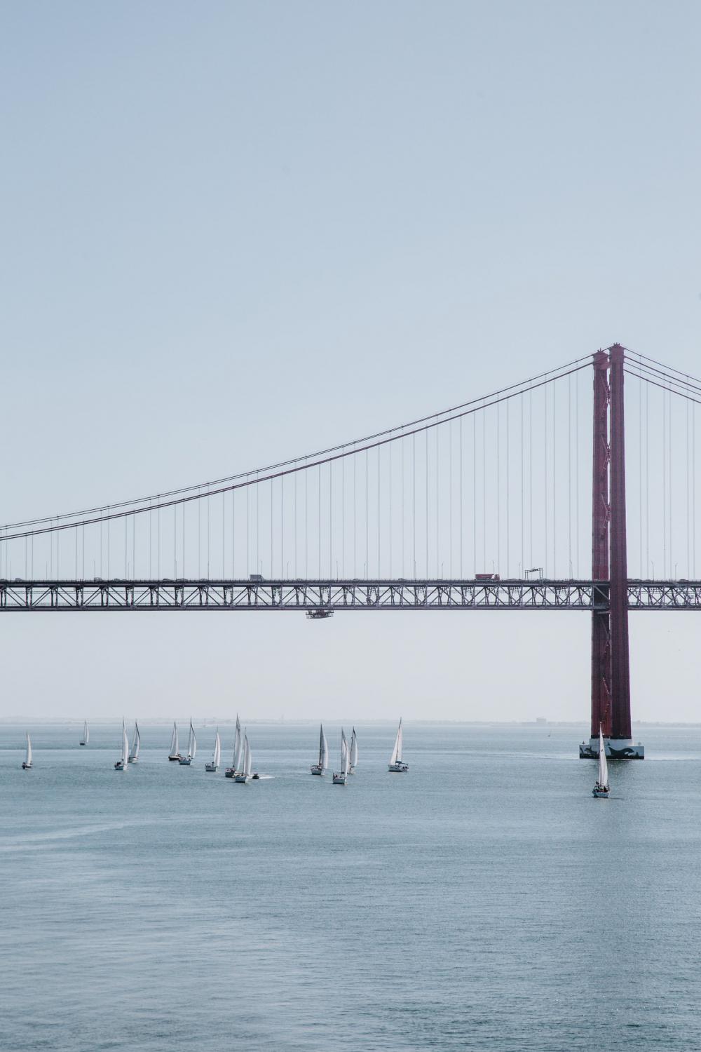Red Suspension Bridge Over Waterway Filled With Sailboats Photo Red Suspension Bridge Over Waterway Filled With Sailboats Photo