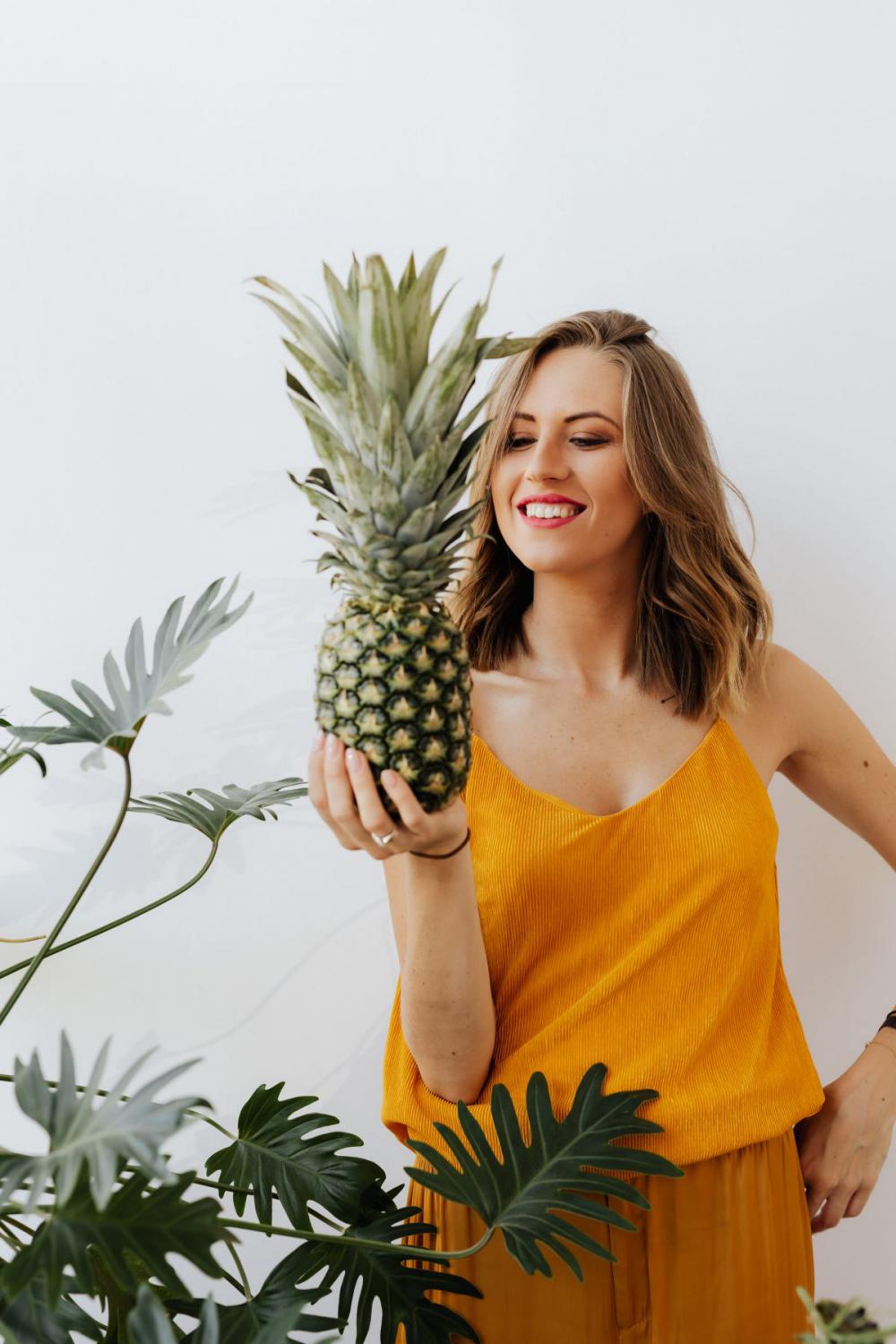 A beautiful smiling young woman is holding a pineapple A beautiful smiling young woman is holding a pineapple