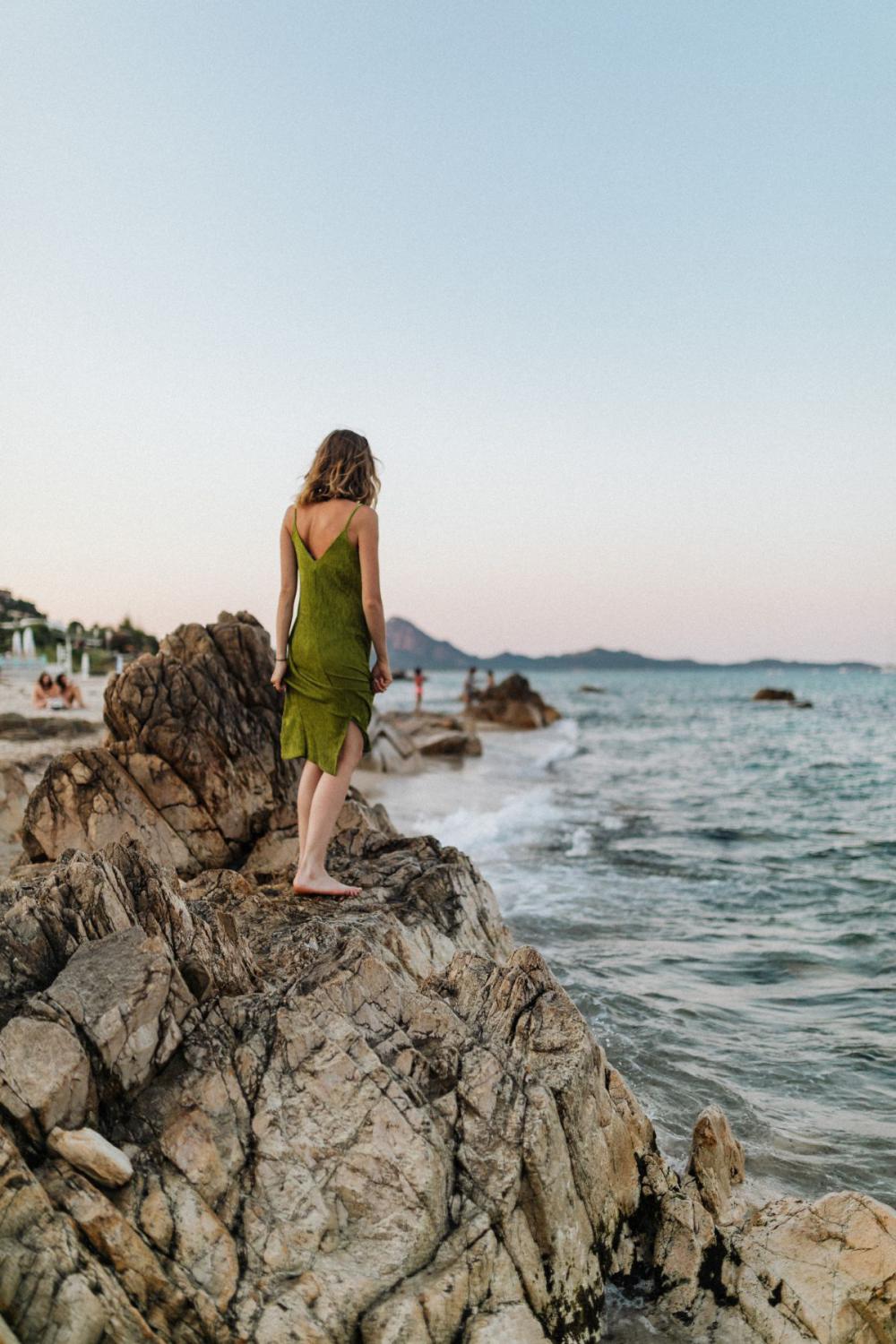 A woman in a green dress on a rock by the sea A woman in a green dress on a rock by the sea