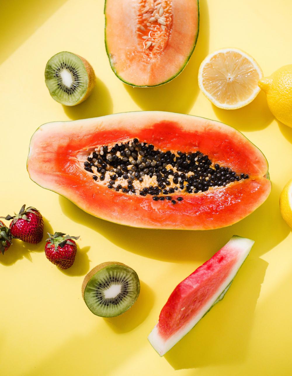 A Papaya Is Surrounded By Fruit On Yellow Background Photo A Papaya Is Surrounded By Fruit On Yellow Background Photo