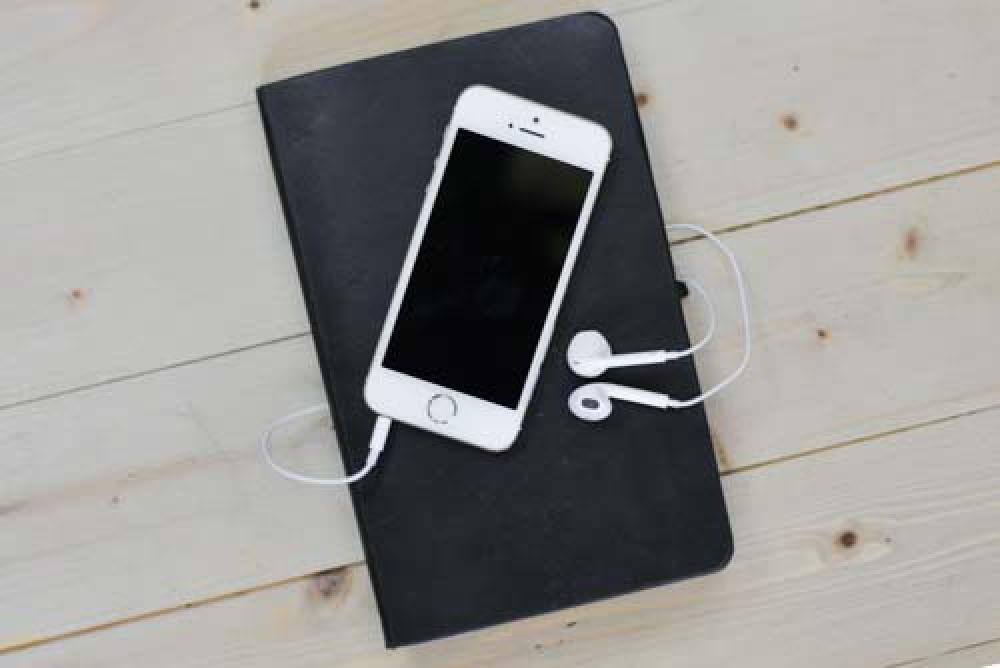 White iPhone On Black Book With Headphones White iPhone On Black Book With Headphones