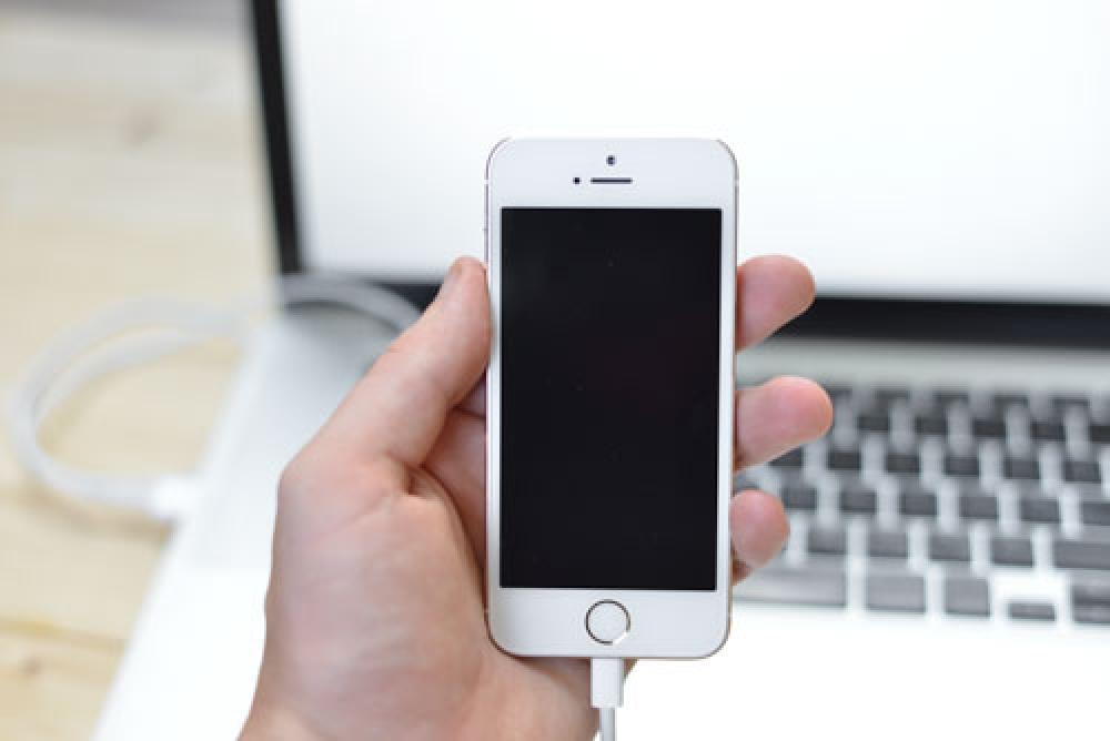 Male Hand Holding iPhone Connected to Laptop Male Hand Holding iPhone Connected to Laptop