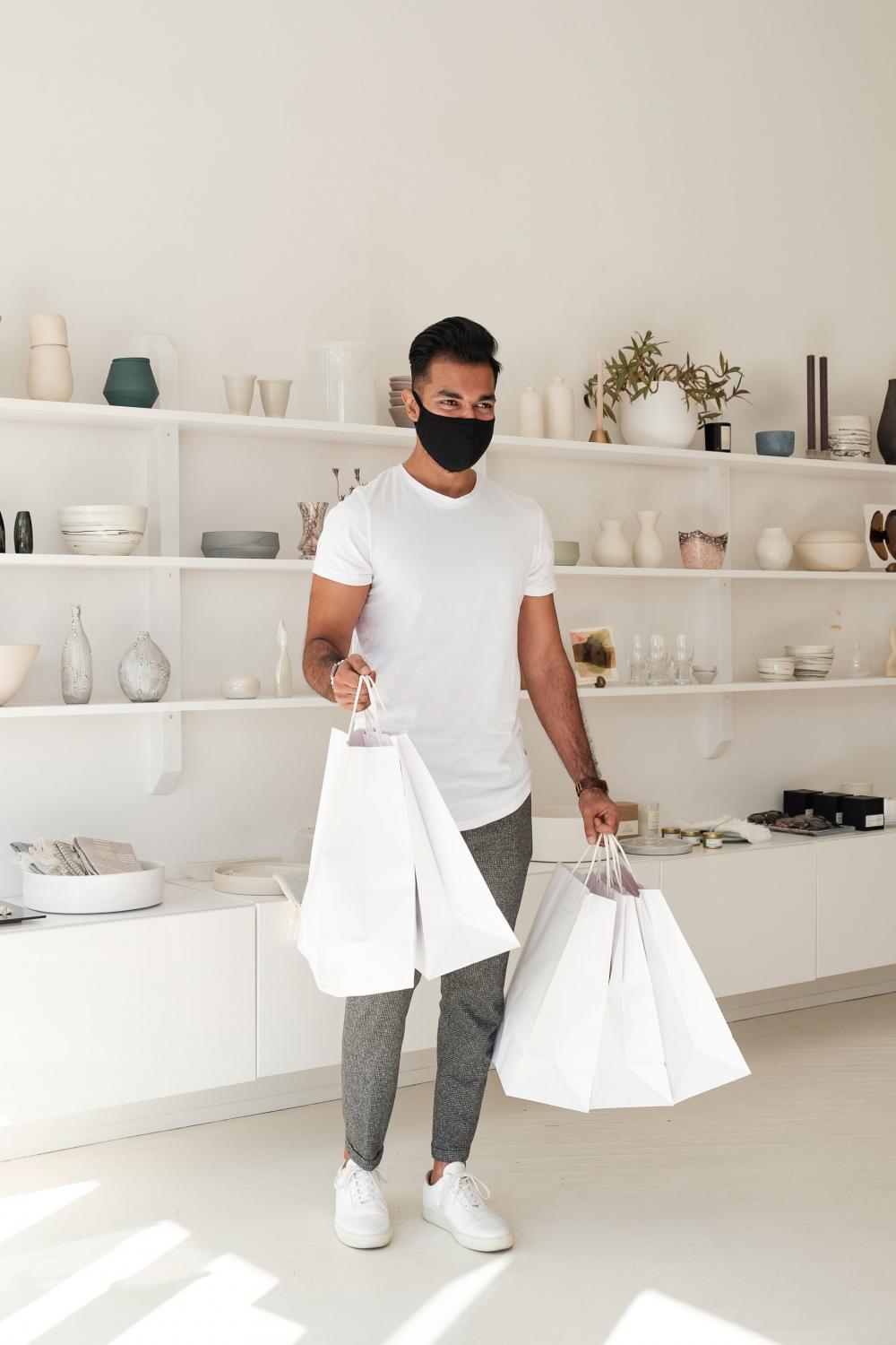 Customer In Face Mask Smiles And Holds White Shopping Bags Photo Customer In Face Mask Smiles And Holds White Shopping Bags Photo