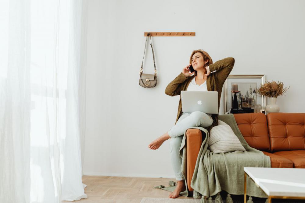 A woman works using a laptop from her couch at home A woman works using a laptop from her couch at home