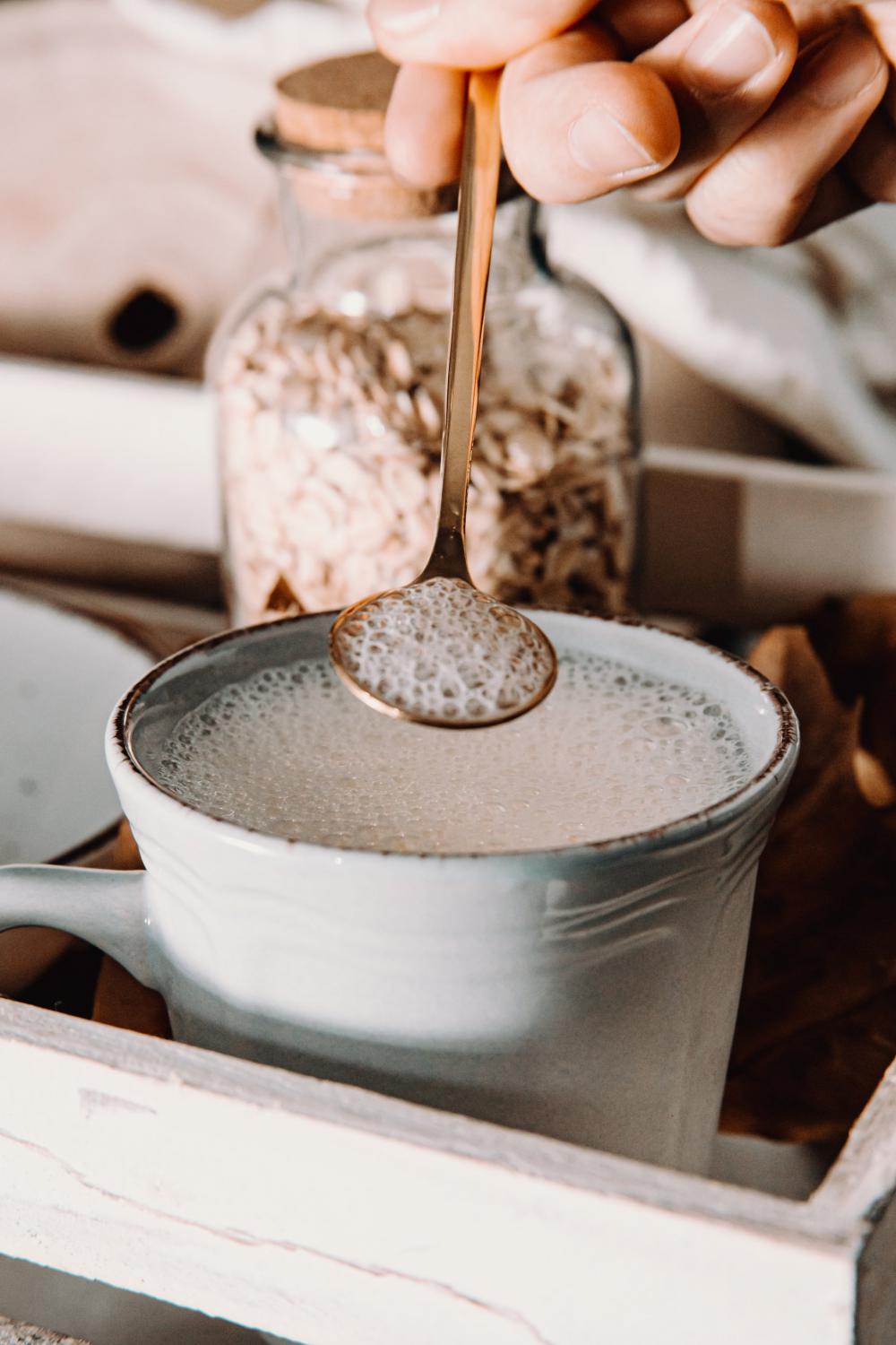 Hand Holds A Gold Spoon Over A Mug Filled With Foamy Milk Photo Hand Holds A Gold Spoon Over A Mug Filled With Foamy Milk Photo