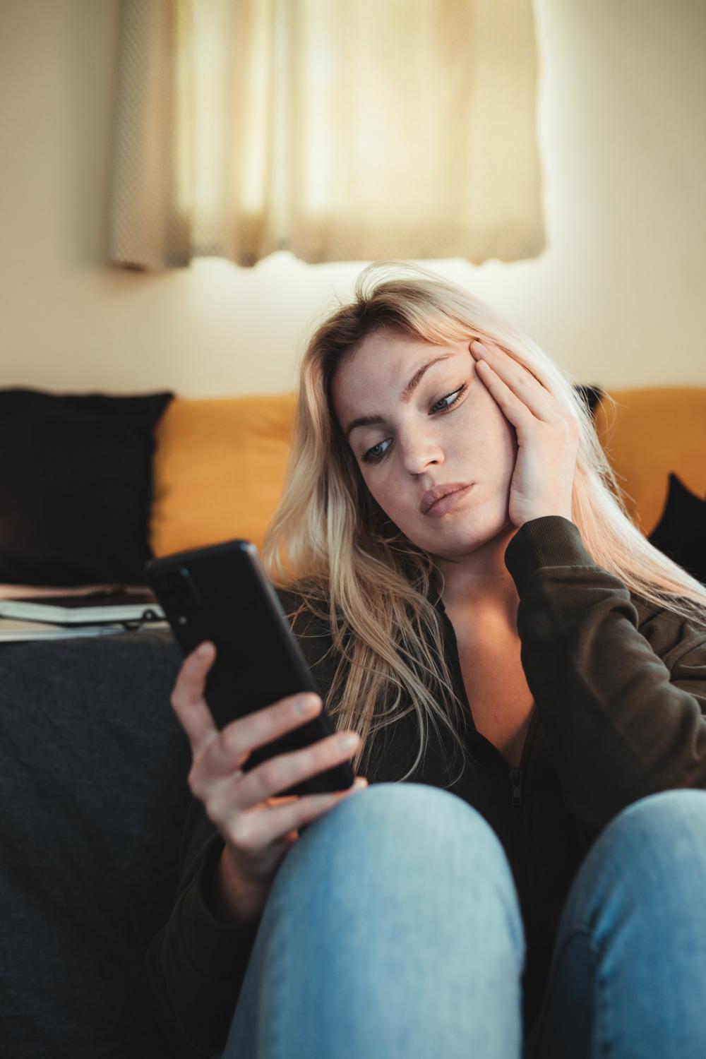 Woman Holds Her Hand To Her Cheek While She Looks At Phone Photo Woman Holds Her Hand To Her Cheek While She Looks At Phone Photo