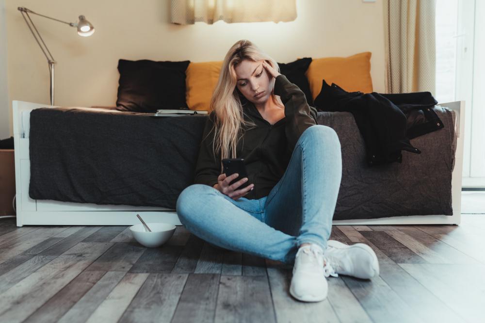 Woman Sits On Floor And Looks At Her Cell Phone Photo Woman Sits On Floor And Looks At Her Cell Phone Photo