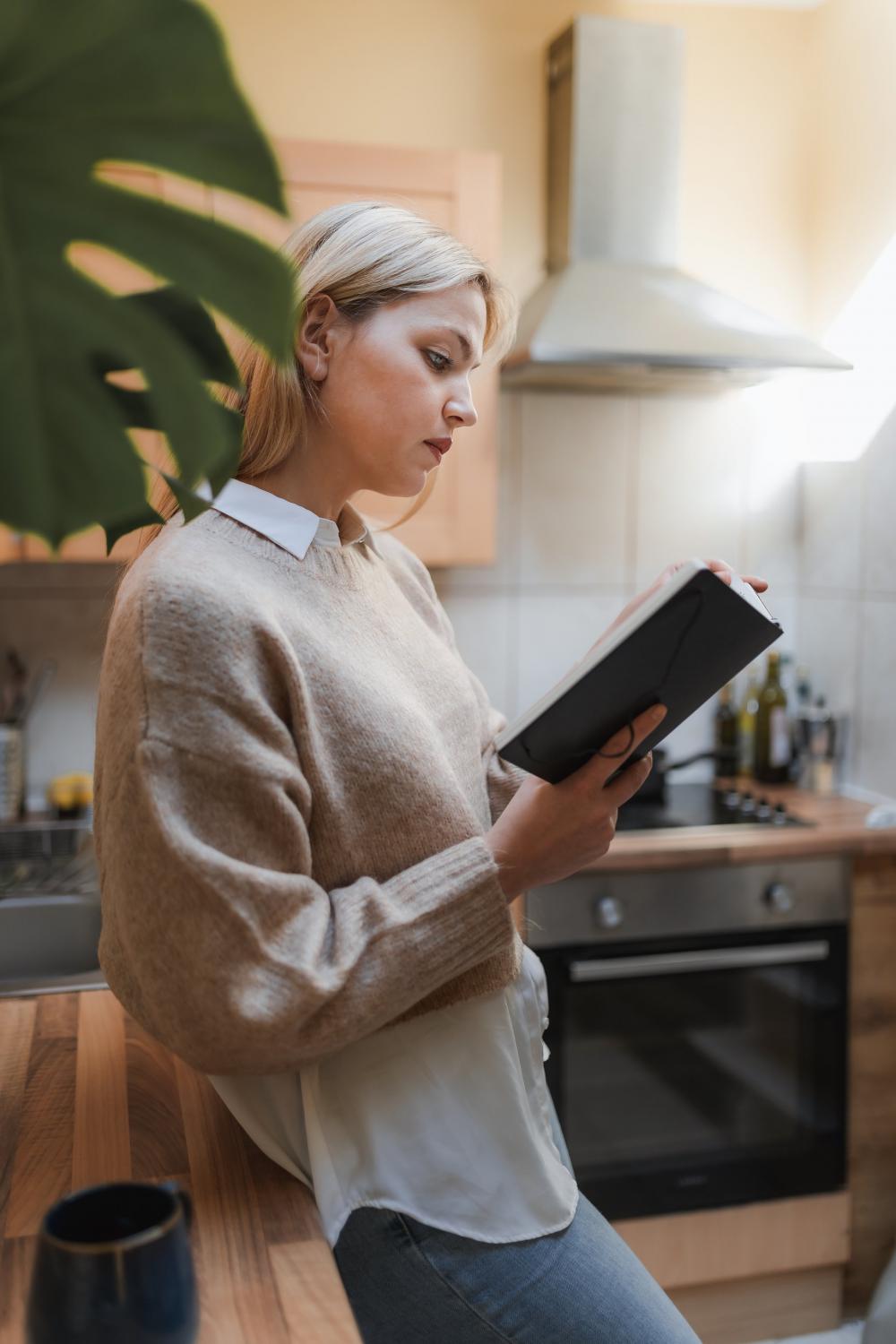 Woman Stands In Her Kitchen Reading A Book Photo Woman Stands In Her Kitchen Reading A Book Photo