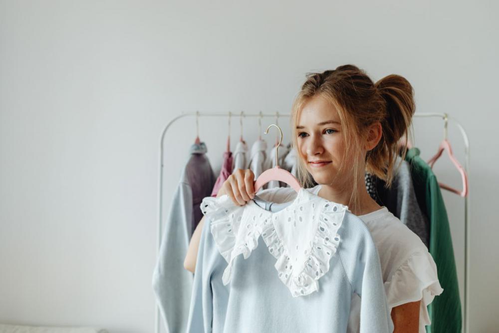 A teenager picks clothes from a hanger in her room A teenager picks clothes from a hanger in her room