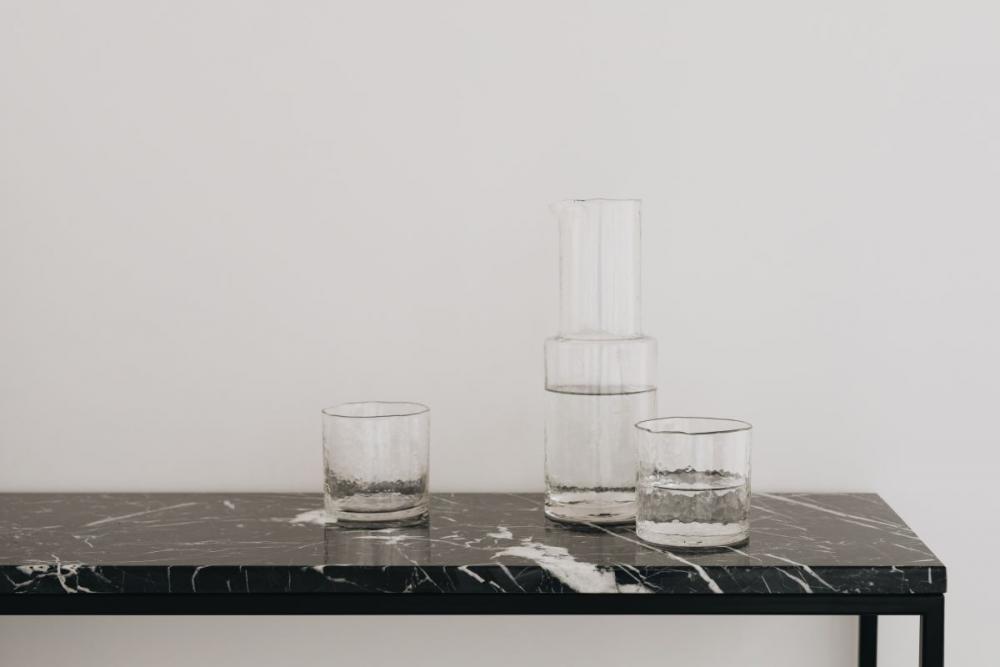 Water in a transparent glass carafe and glasses on a black marble console Water in a transparent glass carafe and glasses on a black marble console