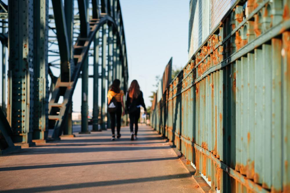 Two females walking across a rusty industrial overpass Two females walking across a rusty industrial overpass
