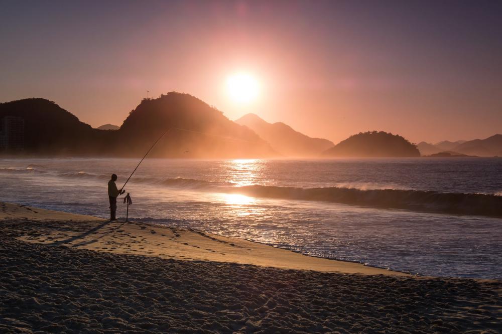Person Fishing On The Beach Is Silhouetted At Sunset Photo Person Fishing On The Beach Is Silhouetted At Sunset Photo