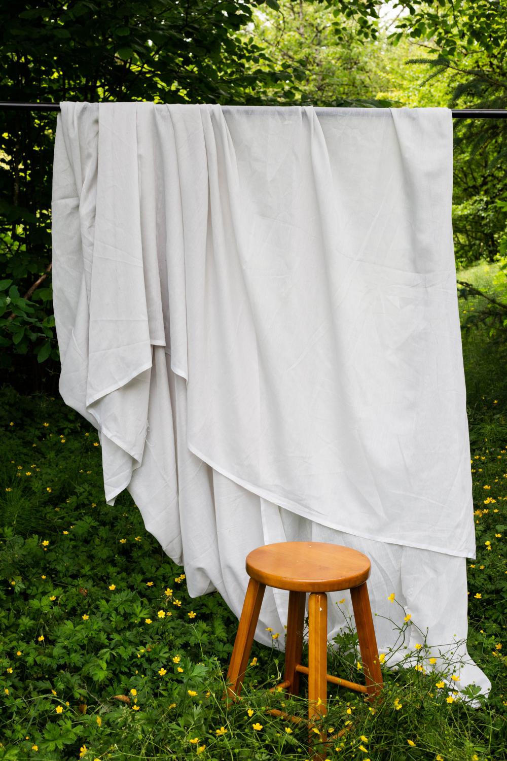 White Flowing Sheet Outdoors With A Wooden Stool In Front Of It Photo White Flowing Sheet Outdoors With A Wooden Stool In Front Of It Photo