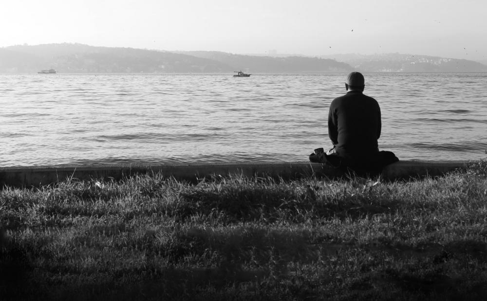 Person Sits Looking Out Towards Still Water Photo Person Sits Looking Out Towards Still Water Photo