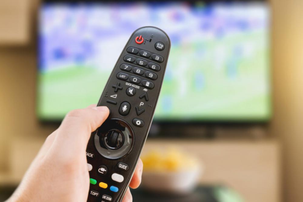 Hand Holding Remote Control with TV Playing in the Background Hand Holding Remote Control with TV Playing in the Background