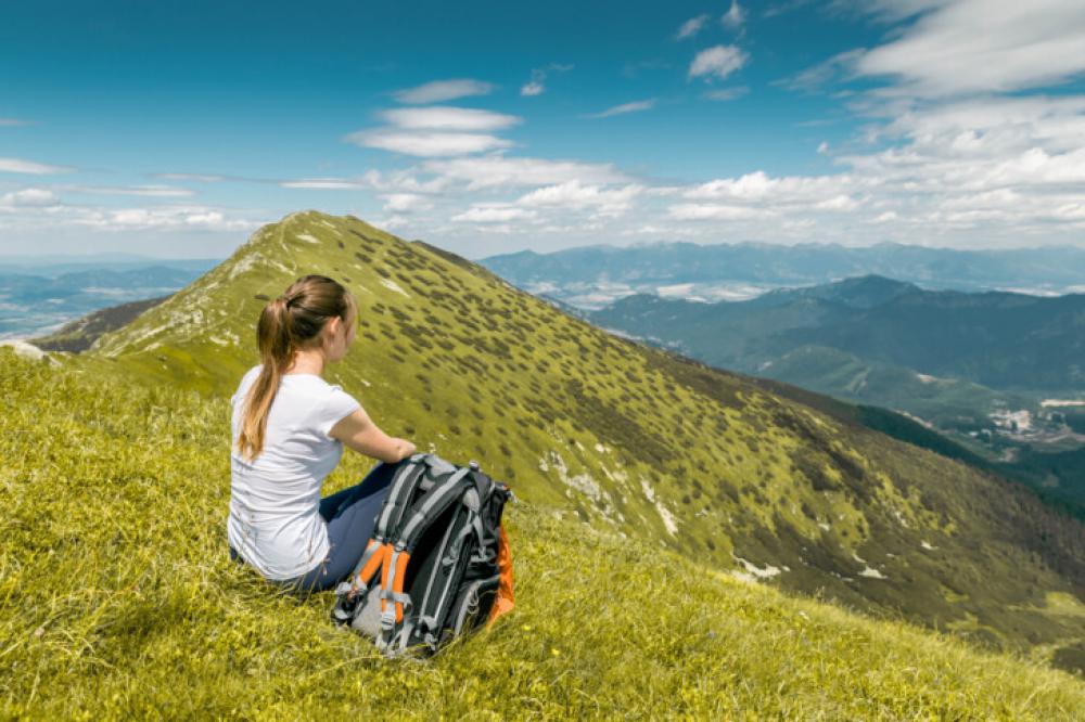 Young Woman Resting with Backpack on Mountain Top with Scenic View Young Woman Resting with Backpack on Mountain Top with Scenic View