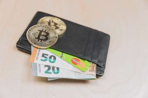 Leather wallet with money and Bitcoin on wooden background