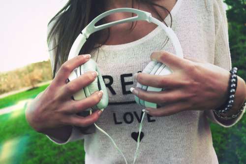 Young woman in white sweater holding headphones in hands