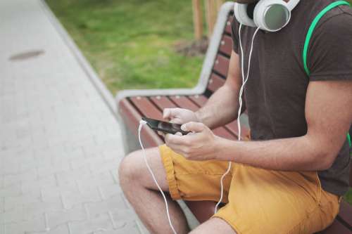 Young boy on a bench in the street listening to music from a mobile phone