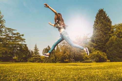 Happy young girl jumping in the park at summer