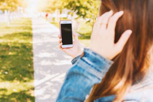 Mockup image of a woman using smartphone with blank black screen at outdoor