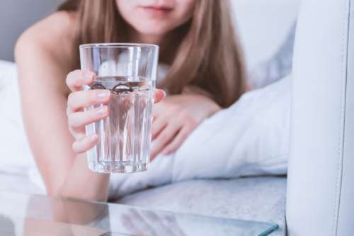 Close up Woman holding glass of water on bed in the morning