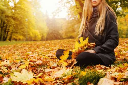 Young woman sitting on a fallen autumn leaves in a park