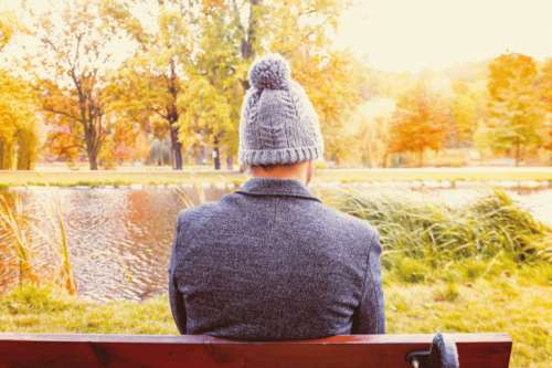 A young man sitting on a bench at the park in autumn