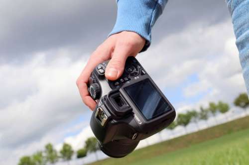 Detail of hand that holds DSLR camera in landscape