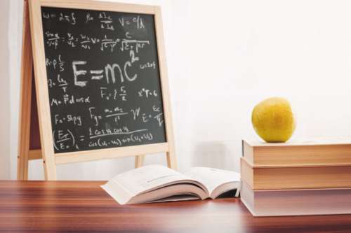 School books with apple on desk over school board background