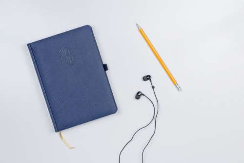 Pretty diary with a pencil and headphones on the white table.