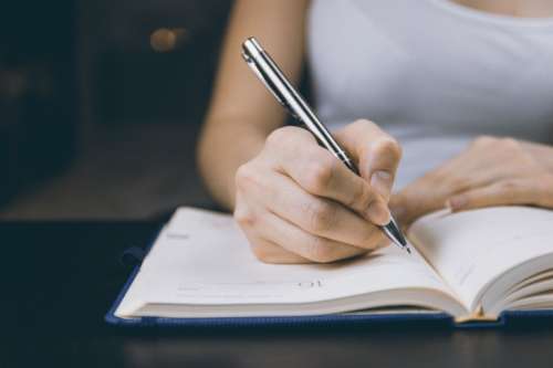 The woman’s hand holds a pencil and writes a plan into a diary at home