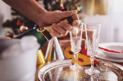 Man Opening Champagne In Room Decorated For Christmas