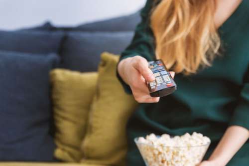 Young girl with TV remote and a popcorn at home