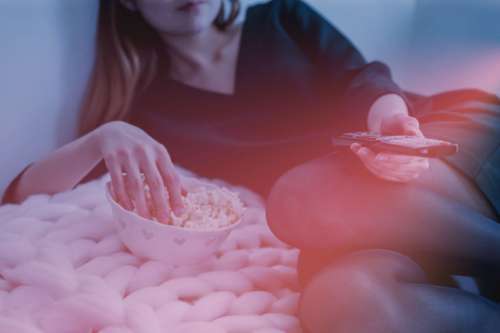 Woman is watching TV and eats a popcorn from bowl